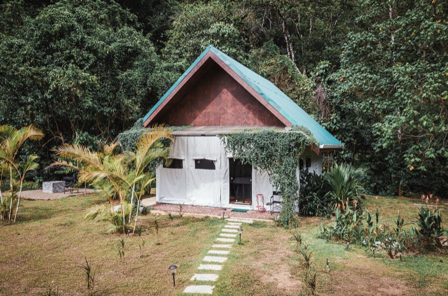 Listing photo of a jungle glamping cabin exterior with a teal roof and stone path
